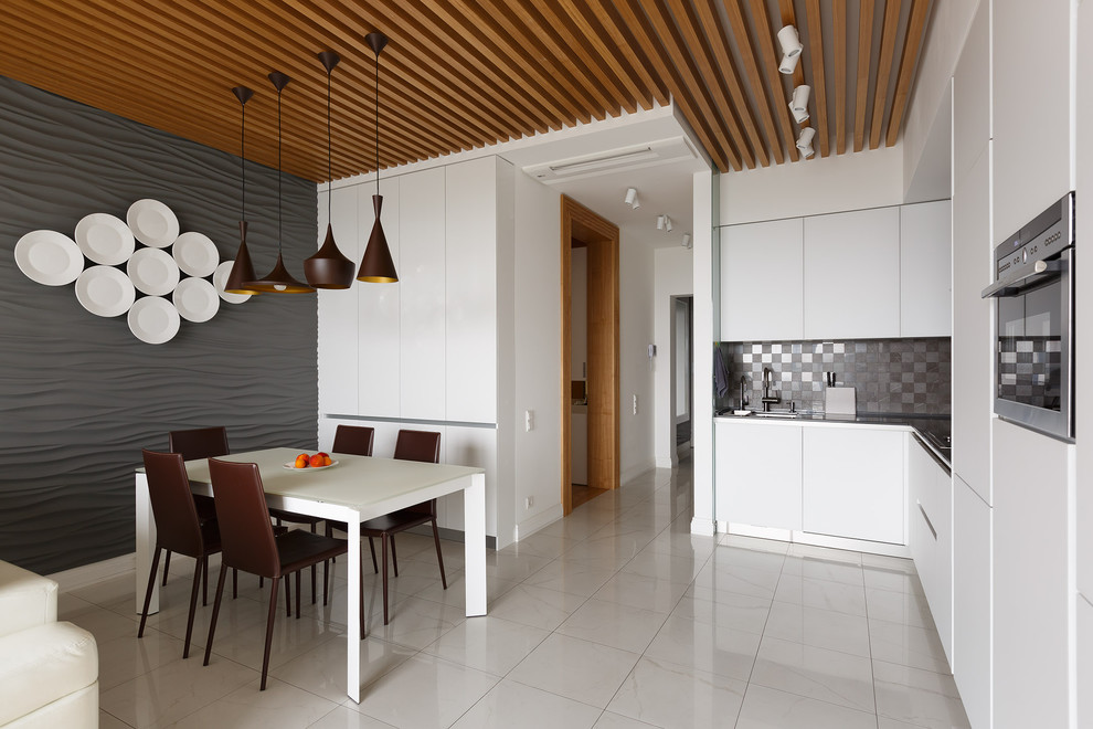 Modern inredning av ett mellanstort kök, med släta luckor, vita skåp, grått stänkskydd, rostfria vitvaror och vitt golv