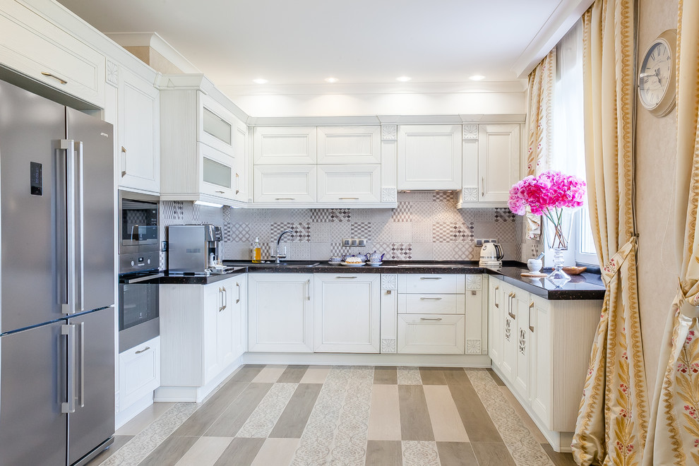 Cette photo montre une cuisine tendance en U avec un évier posé, des portes de placard blanches, une crédence grise, un électroménager en acier inoxydable et un sol beige.