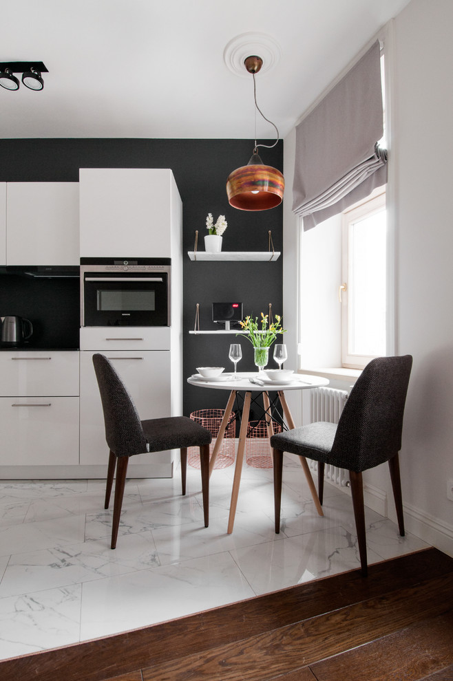 Свежая идея для дизайна: прямая кухня-гостиная в скандинавском стиле с плоскими фасадами, белыми фасадами, черным фартуком, черной техникой и мраморным полом без острова - отличное фото интерьера