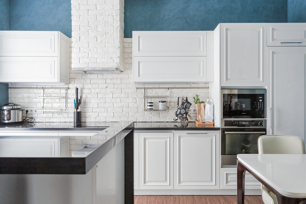 Cette photo montre une cuisine ouverte linéaire tendance avec un placard avec porte à panneau surélevé, des portes de placard blanches, une crédence blanche, un électroménager en acier inoxydable et îlot.