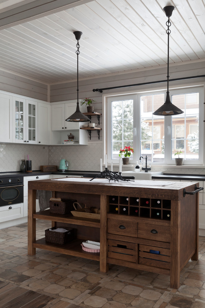 Cette photo montre une cuisine scandinave en L avec un évier de ferme, un placard à porte shaker, des portes de placard blanches, une crédence blanche, un électroménager noir, îlot et un sol marron.