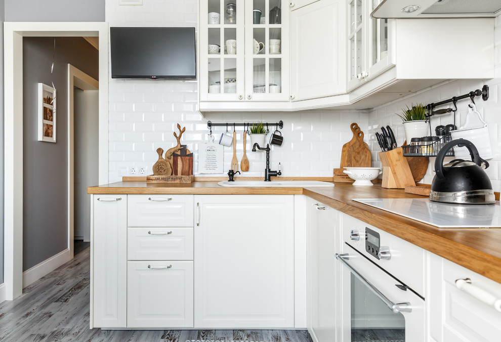 モスクワにある北欧スタイルのおしゃれなキッチン (ドロップインシンク、レイズドパネル扉のキャビネット、白いキャビネット、木材カウンター、白いキッチンパネル、サブウェイタイルのキッチンパネル、白い調理設備、濃色無垢フローリング、アイランドなし、グレーの床、茶色いキッチンカウンター) の写真