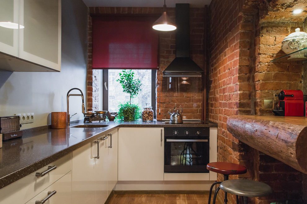 Foto de cocina urbana con fregadero bajoencimera, armarios con paneles lisos, puertas de armario blancas, electrodomésticos negros y suelo de madera en tonos medios