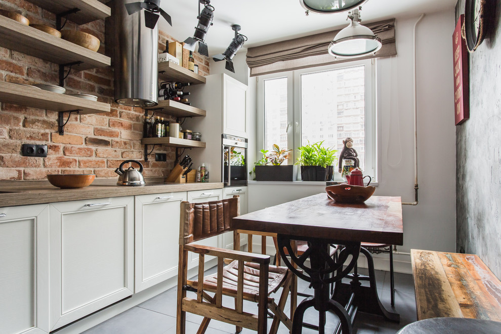 Industriell inredning av ett avskilt linjärt kök, med luckor med infälld panel, vita skåp, brunt stänkskydd, stänkskydd i tegel, rostfria vitvaror och grått golv