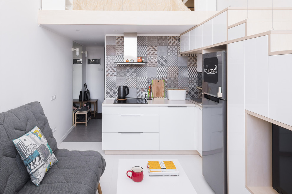 Пример оригинального дизайна: угловая кухня-гостиная в скандинавском стиле с накладной мойкой, плоскими фасадами, белыми фасадами, серым фартуком, светлым паркетным полом и белым полом без острова