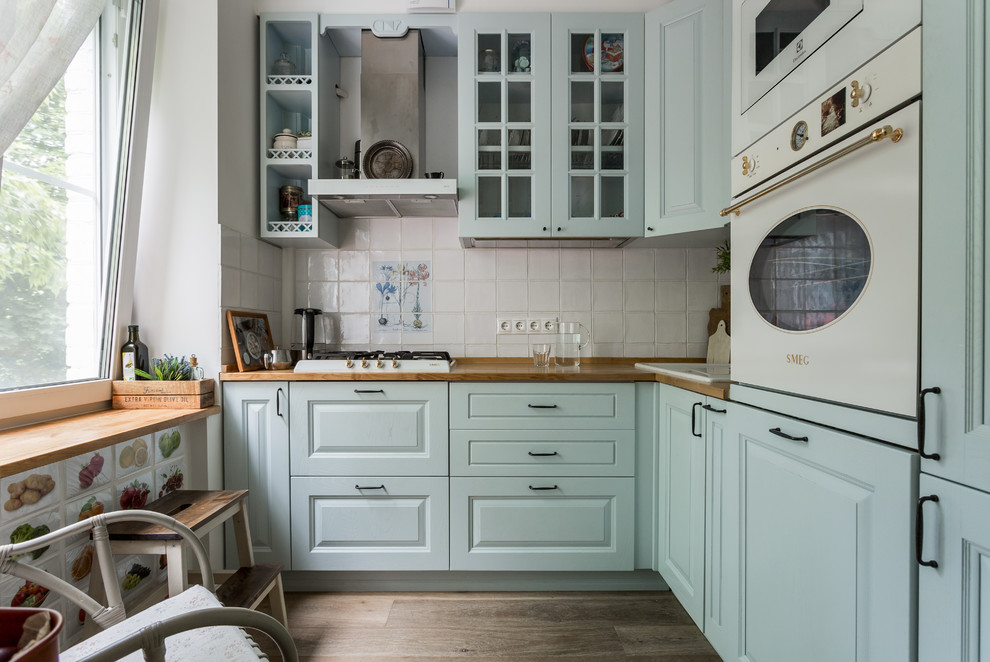 Immagine di una cucina a L minimal con lavello da incasso, ante con bugna sagomata, top in legno, paraspruzzi bianco e elettrodomestici bianchi