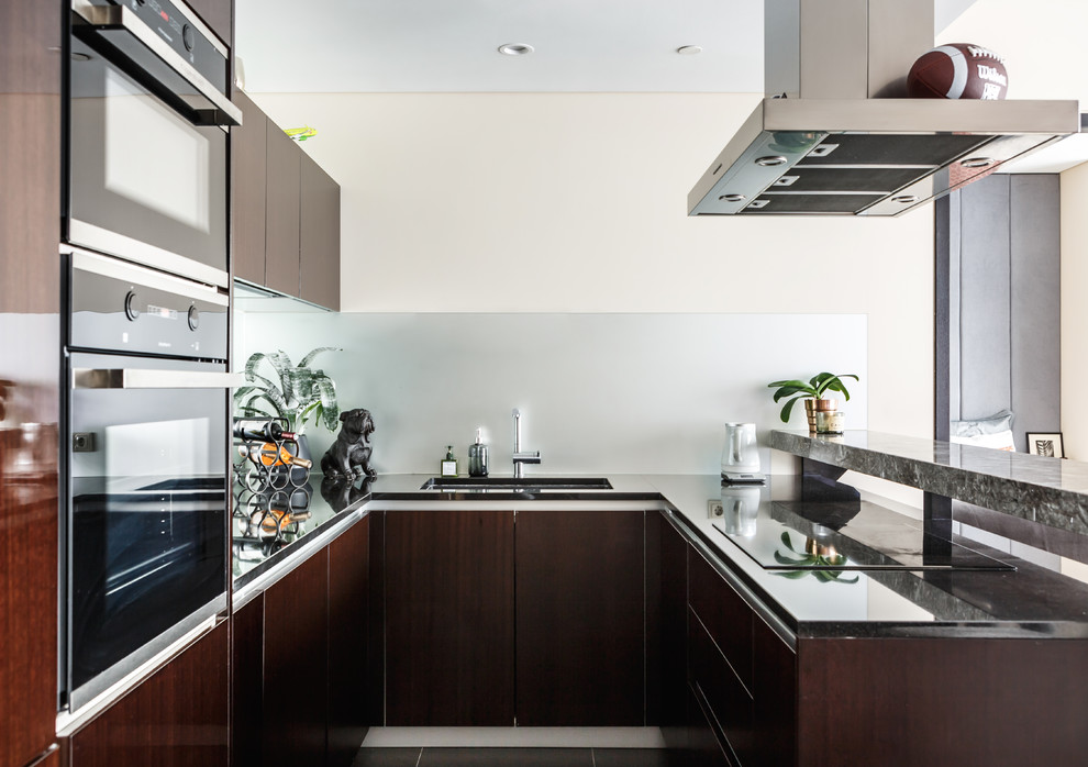 Стильный дизайн: п-образная кухня-гостиная в современном стиле с плоскими фасадами, темными деревянными фасадами, черной техникой и полуостровом - последний тренд