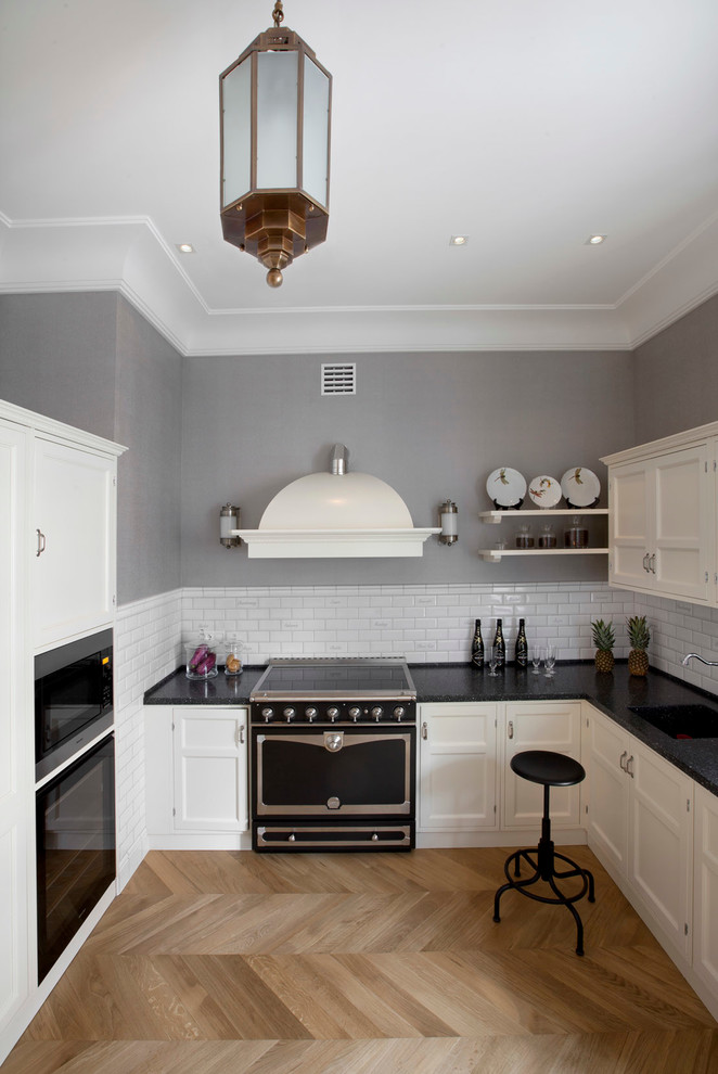 Classic grey and white l-shaped kitchen in Moscow with a single-bowl sink, recessed-panel cabinets, white splashback, ceramic splashback, black appliances, light hardwood flooring and no island.