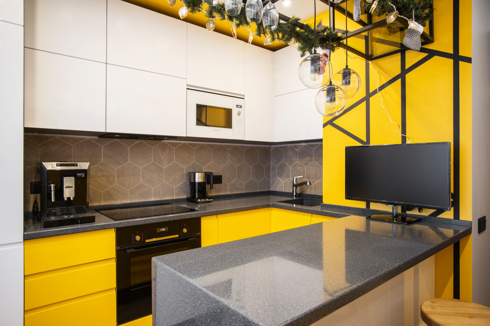 Свежая идея для дизайна: п-образная кухня в современном стиле с врезной мойкой, плоскими фасадами, желтыми фасадами, бежевым фартуком, черной техникой, полуостровом и серой столешницей - отличное фото интерьера