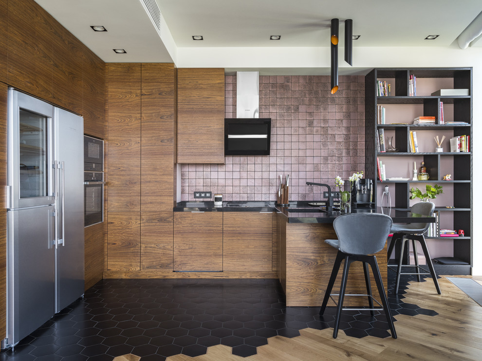 Cette photo montre une cuisine tendance en U et bois brun avec un évier encastré, un placard à porte plane, une crédence rose, un électroménager noir, une péninsule, un sol noir et plan de travail noir.