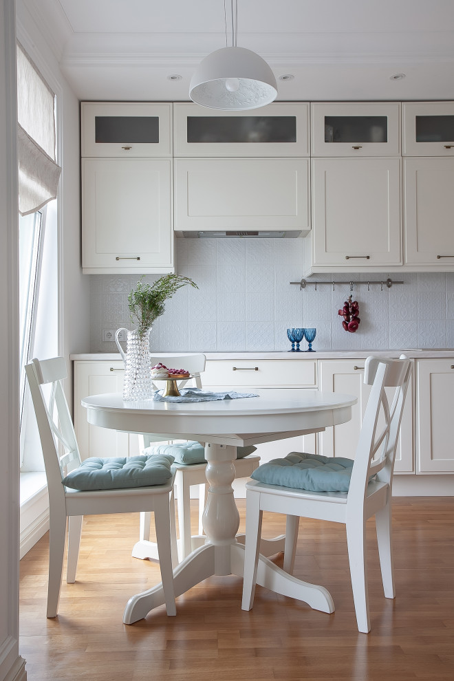 Example of a danish brown floor and medium tone wood floor eat-in kitchen design in Saint Petersburg with white cabinets, white backsplash, white countertops and shaker cabinets