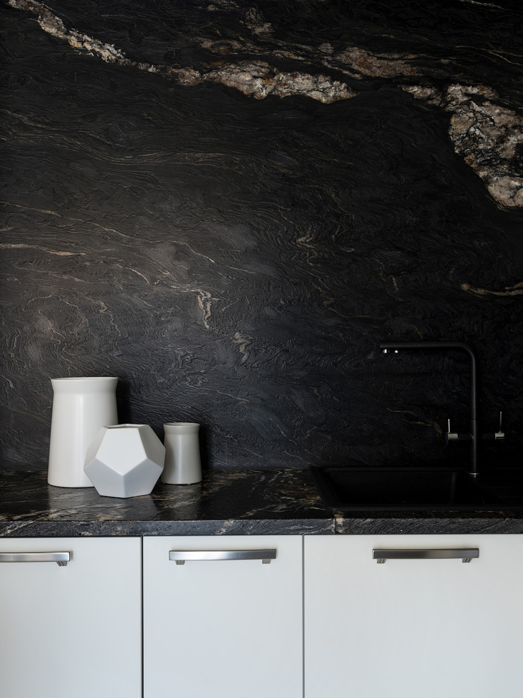 Exempel på ett litet modernt svart svart kök, med en enkel diskho, släta luckor, vita skåp, granitbänkskiva, svart stänkskydd, stänkskydd i sten, vita vitvaror, klinkergolv i porslin, en halv köksö och vitt golv