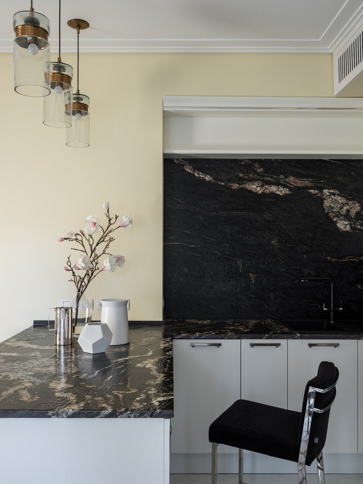 Modern inredning av ett litet svart svart kök, med en enkel diskho, släta luckor, vita skåp, granitbänkskiva, svart stänkskydd, stänkskydd i sten, vita vitvaror, klinkergolv i porslin, en halv köksö och vitt golv