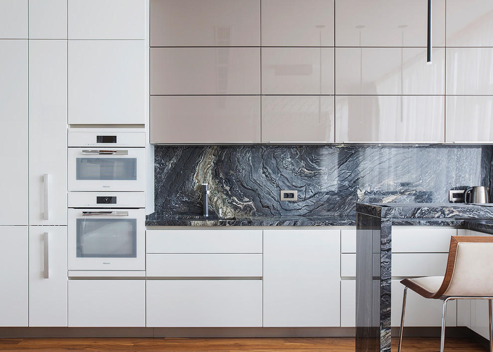 This is an example of a contemporary u-shaped open plan kitchen in Moscow with flat-panel cabinets, black splashback, white appliances, medium hardwood flooring and brown floors.