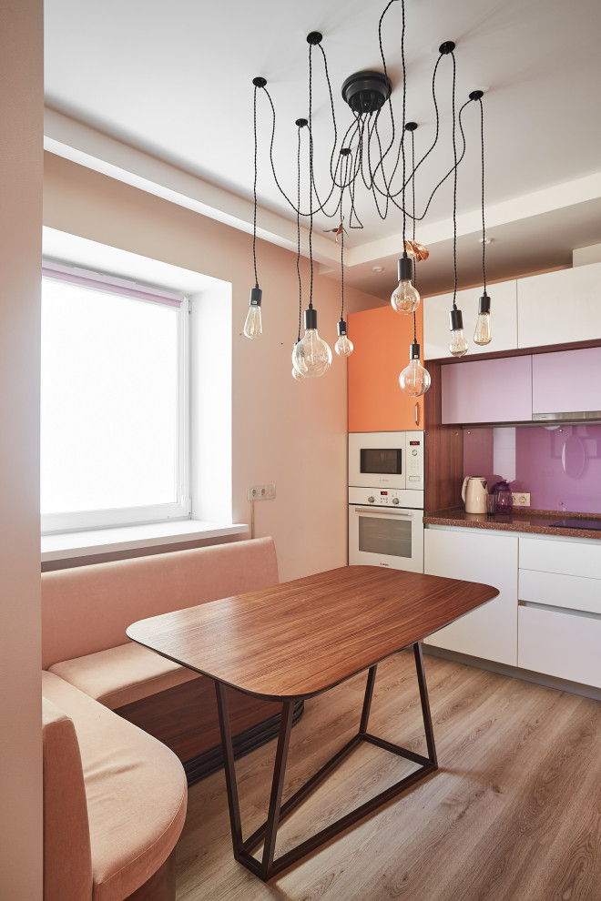Modern inredning av ett mellanstort brun linjärt brunt kök och matrum, med en enkel diskho, släta luckor, orange skåp, bänkskiva i koppar, glaspanel som stänkskydd, vita vitvaror, laminatgolv och brunt golv