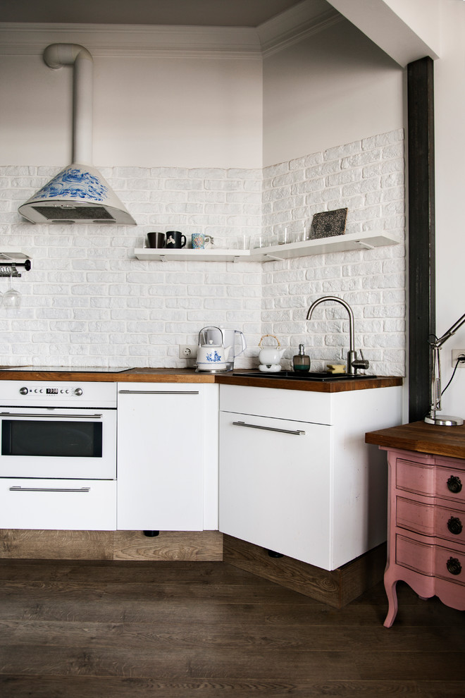 Inredning av ett modernt kök, med en nedsänkt diskho, släta luckor, vita skåp, träbänkskiva, vita vitvaror och mörkt trägolv