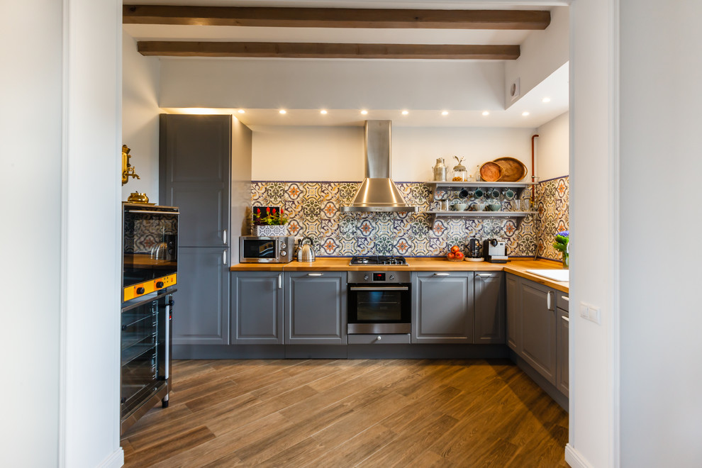 Aménagement d'une cuisine méditerranéenne en L avec un évier posé, un placard avec porte à panneau surélevé, des portes de placard grises, une crédence multicolore, un électroménager en acier inoxydable et un sol marron.