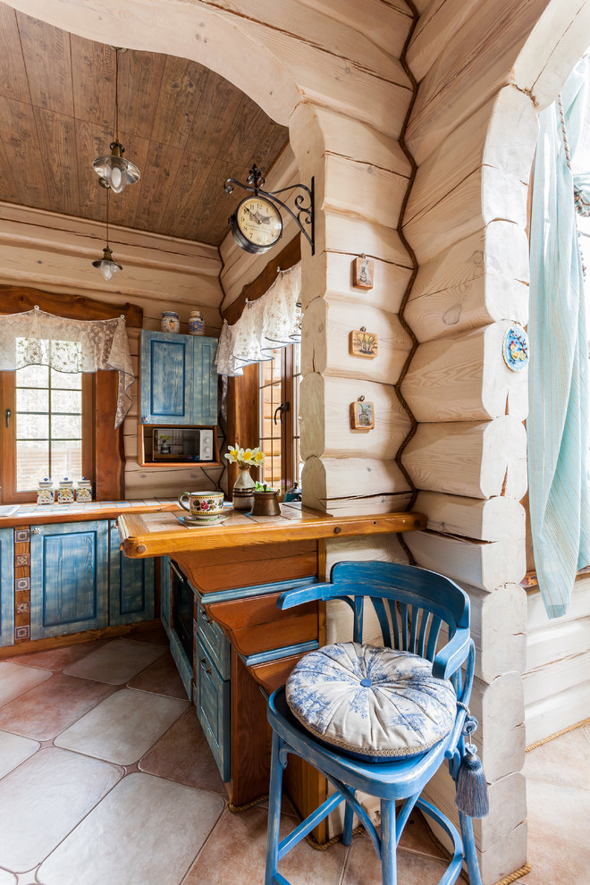 Cette image montre une cuisine style shabby chic en U avec un évier posé, un placard avec porte à panneau surélevé, des portes de placard bleues, plan de travail carrelé et une péninsule.