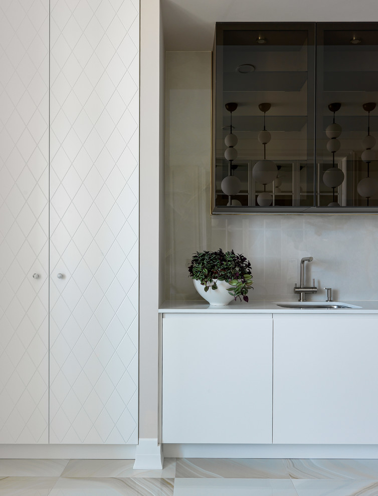 Cette image montre une cuisine design avec un évier encastré, un placard à porte plane, des portes de placard blanches, une crédence beige, un sol beige et un plan de travail blanc.