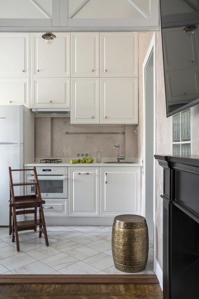 Modelo de cocina lineal clásica renovada con armarios con paneles con relieve, puertas de armario blancas, salpicadero beige, electrodomésticos blancos, suelo blanco y encimeras blancas