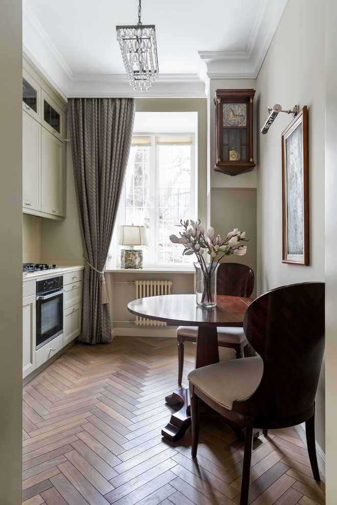 This is an example of a traditional single-wall enclosed kitchen in Moscow with recessed-panel cabinets, white cabinets, black appliances, medium hardwood flooring, no island and brown floors.