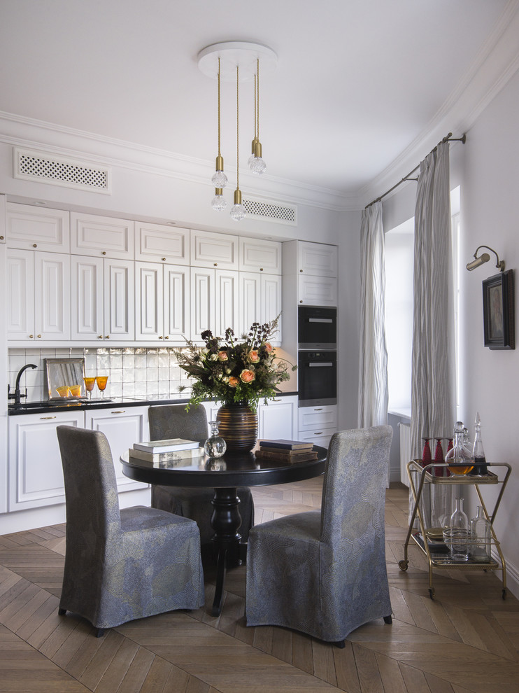 This is an example of a traditional single-wall kitchen in Moscow with raised-panel cabinets, white cabinets, white splashback, stainless steel appliances, medium hardwood flooring, no island and brown floors.