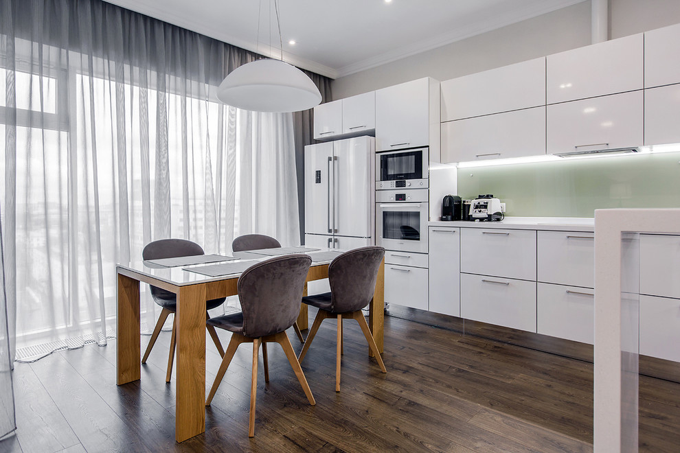 Свежая идея для дизайна: п-образная кухня-гостиная в скандинавском стиле с плоскими фасадами, белыми фасадами, зеленым фартуком, белой техникой, темным паркетным полом и полуостровом - отличное фото интерьера