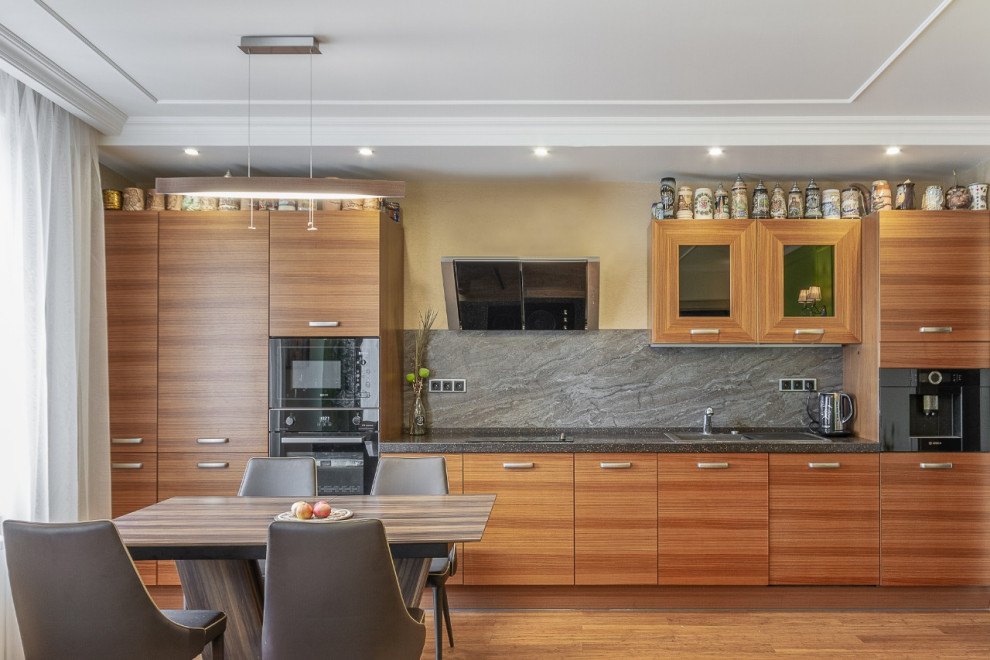Idéer för att renovera ett mellanstort funkis grå linjärt grått kök och matrum, med en nedsänkt diskho, släta luckor, skåp i mellenmörkt trä, grått stänkskydd, svarta vitvaror och mellanmörkt trägolv