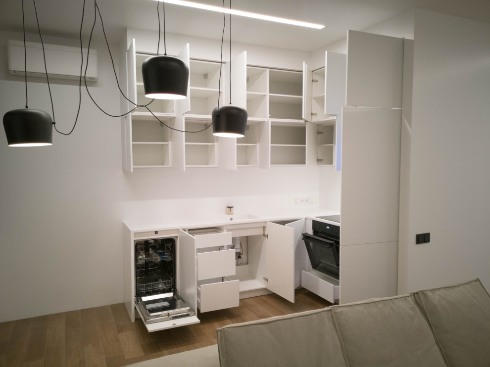 Foto på ett litet funkis vit kök, med en undermonterad diskho, vita skåp, bänkskiva i koppar, vitt stänkskydd, svarta vitvaror, ljust trägolv och flerfärgat golv