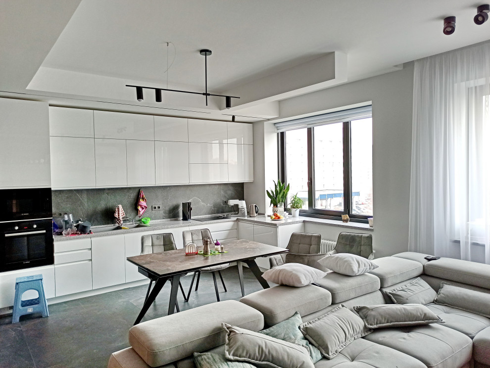Immagine di una cucina design con lavello sottopiano, ante lisce, ante bianche, paraspruzzi grigio, elettrodomestici neri, pavimento grigio e top grigio
