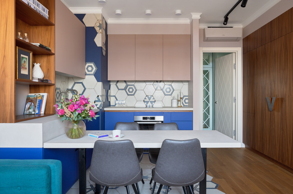 Foto på ett funkis vit kök, med blå skåp, vitt stänkskydd, rostfria vitvaror och en halv köksö
