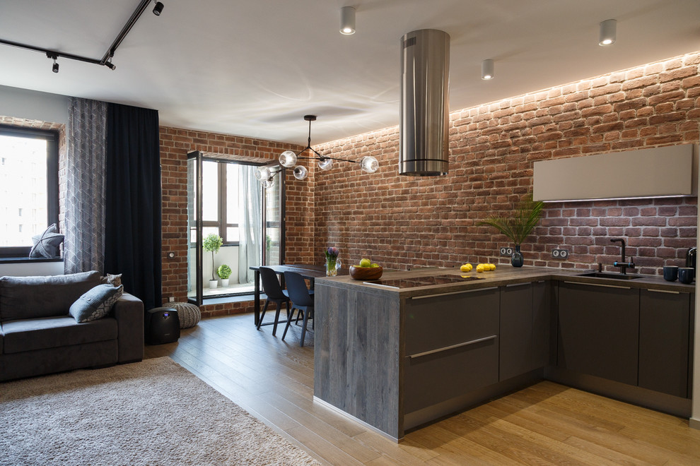 Modern inredning av ett grå grått kök, med släta luckor, grå skåp, brunt stänkskydd, mellanmörkt trägolv, en halv köksö och brunt golv