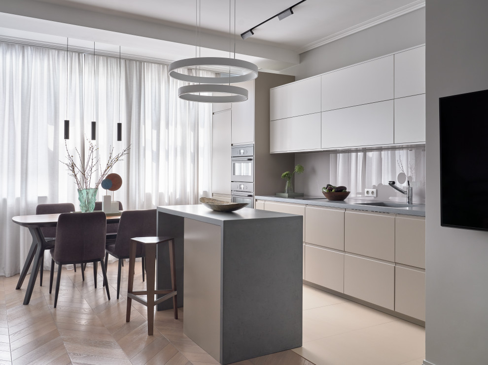 Стильный дизайн: светлая кухня-гостиная в современном стиле с монолитной мойкой, плоскими фасадами, белыми фасадами, островом, бежевым полом и двухцветным гарнитуром - последний тренд