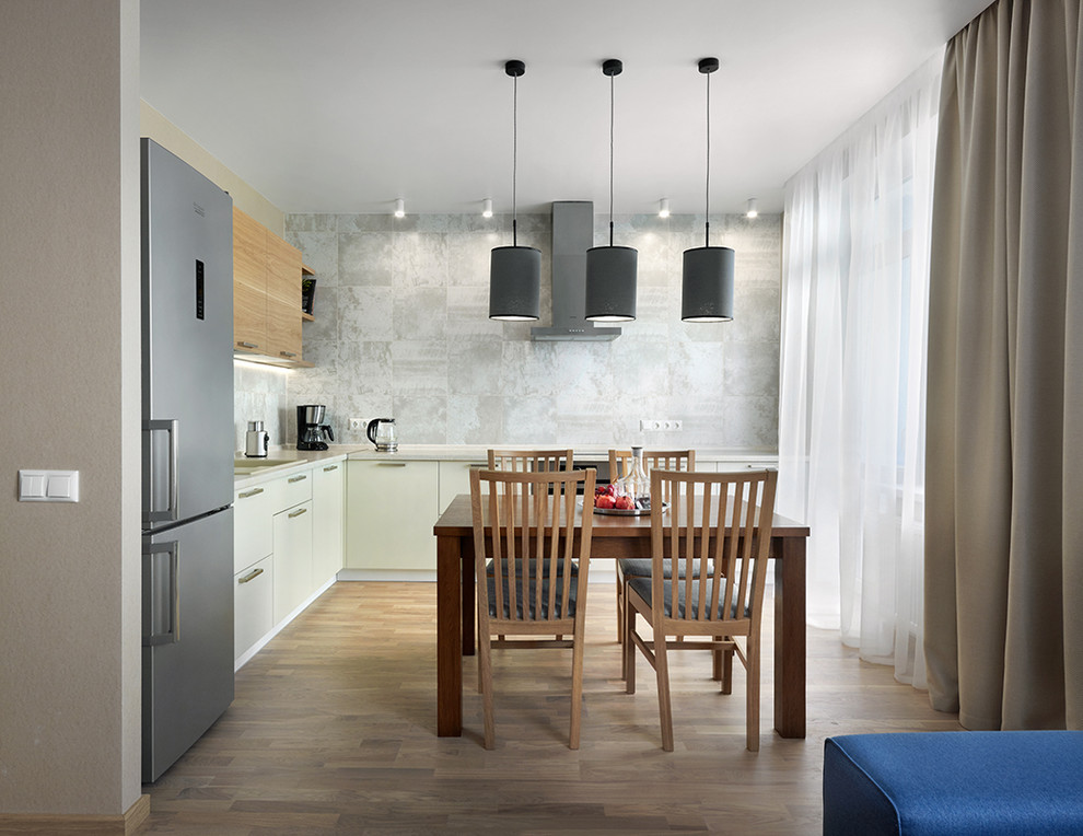 Идея дизайна: угловая кухня-гостиная в современном стиле с накладной мойкой, плоскими фасадами, серым фартуком и светлым паркетным полом