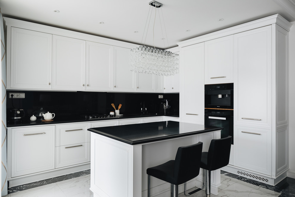 На фото: угловая, светлая кухня-гостиная в стиле неоклассика (современная классика) с фасадами с утопленной филенкой, белыми фасадами, черным фартуком, черной техникой, островом, разноцветным полом и черной столешницей с