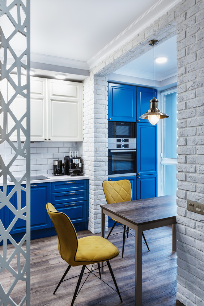 Inspiration for a medium sized urban l-shaped open plan kitchen in Moscow with an integrated sink, raised-panel cabinets, blue cabinets, composite countertops, white splashback, ceramic splashback, stainless steel appliances, laminate floors, no island, brown floors and white worktops.