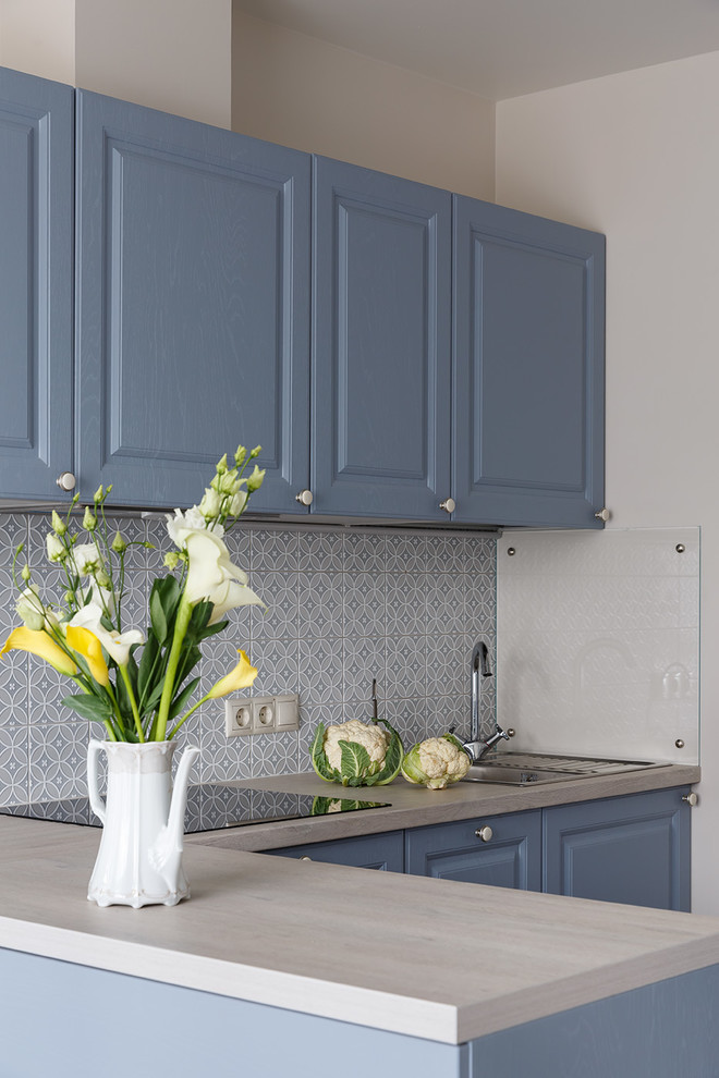 Immagine di una cucina a L minimal con lavello da incasso, ante con bugna sagomata, ante blu, paraspruzzi grigio, penisola e top beige