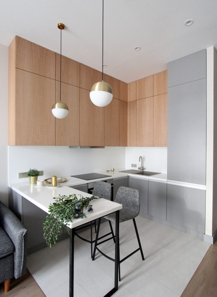 Foto di una cucina ad U design con ante lisce, ante in legno chiaro, paraspruzzi bianco, penisola, pavimento grigio e top bianco