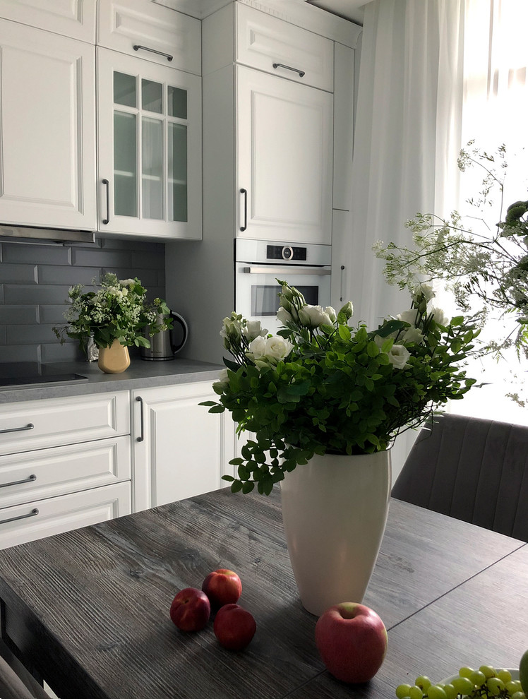 Свежая идея для дизайна: маленькая угловая кухня в стиле неоклассика (современная классика) с фасадами с утопленной филенкой, белыми фасадами и серым полом для на участке и в саду - отличное фото интерьера