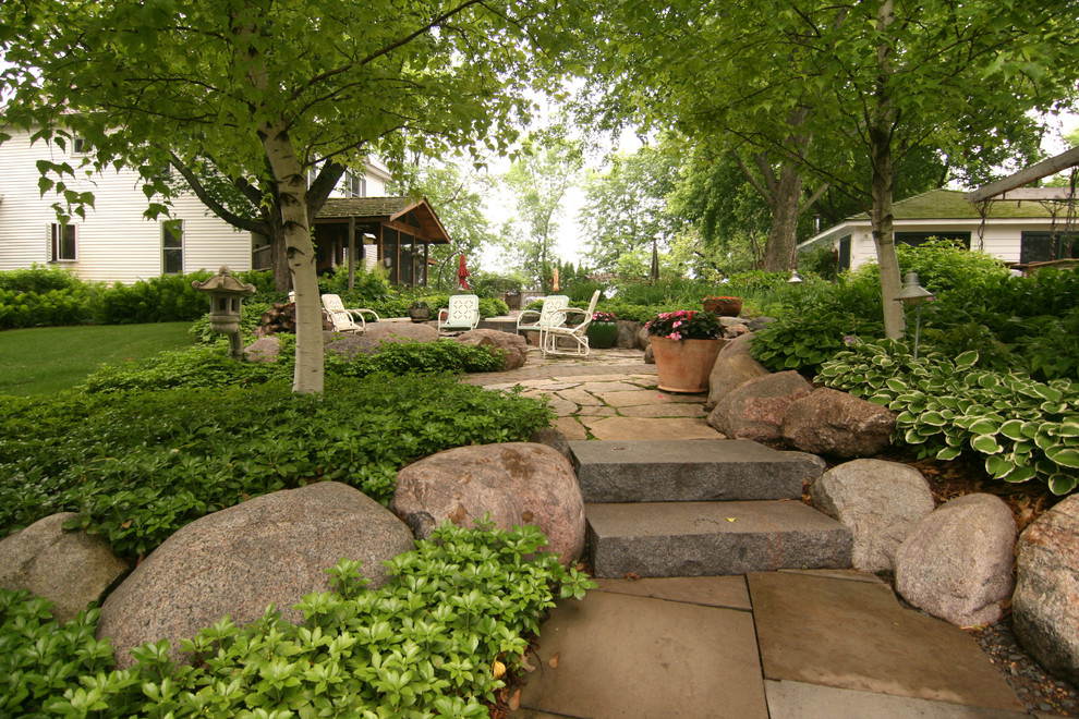 На фото: огромный солнечный регулярный сад на заднем дворе в стиле кантри с подпорной стенкой, хорошей освещенностью и покрытием из каменной брусчатки с