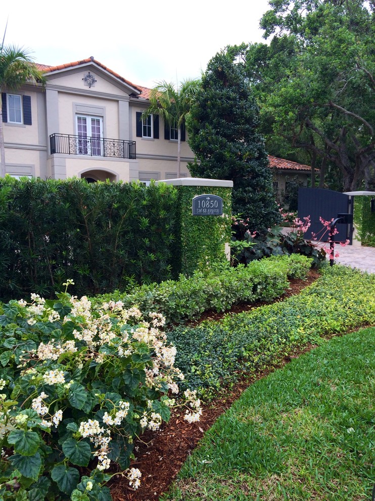 На фото: большой летний регулярный сад на переднем дворе в классическом стиле с полуденной тенью и покрытием из каменной брусчатки