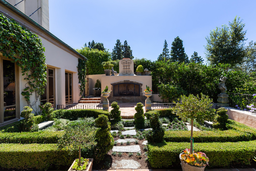 Immagine di un ampio giardino formale esposto in pieno sole dietro casa con un caminetto e pavimentazioni in pietra naturale
