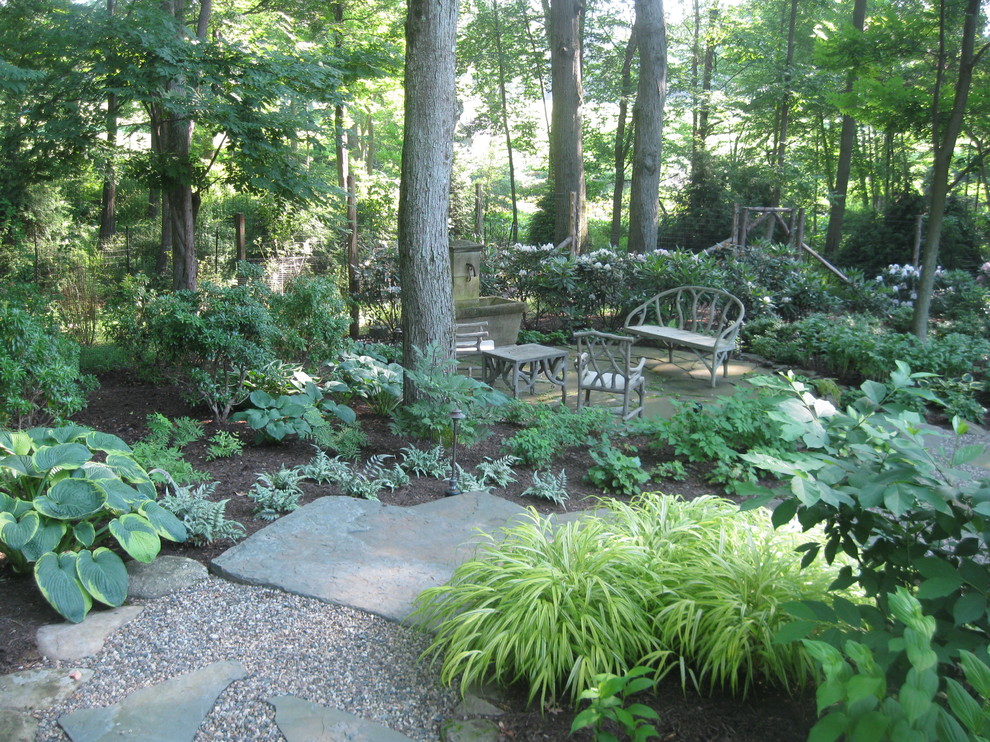Réalisation d'un jardin arrière tradition avec un point d'eau et des pavés en pierre naturelle.