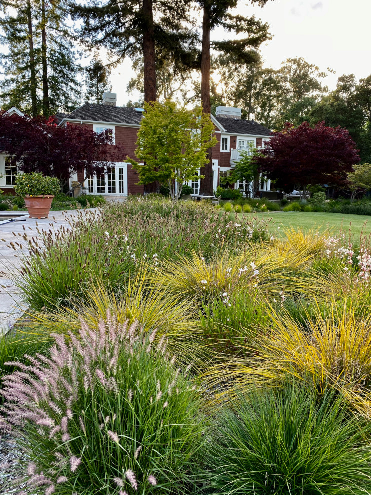 Cette image montre un grand jardin arrière design l'été avec une exposition partiellement ombragée et des pavés en pierre naturelle.