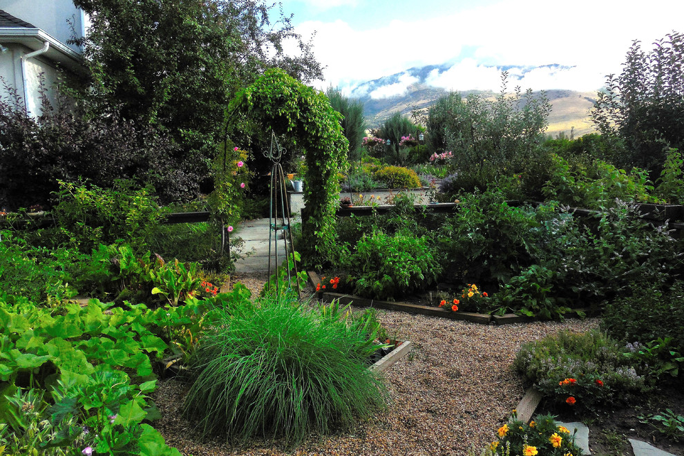 Foto di un grande giardino classico esposto in pieno sole dietro casa in estate con ghiaia