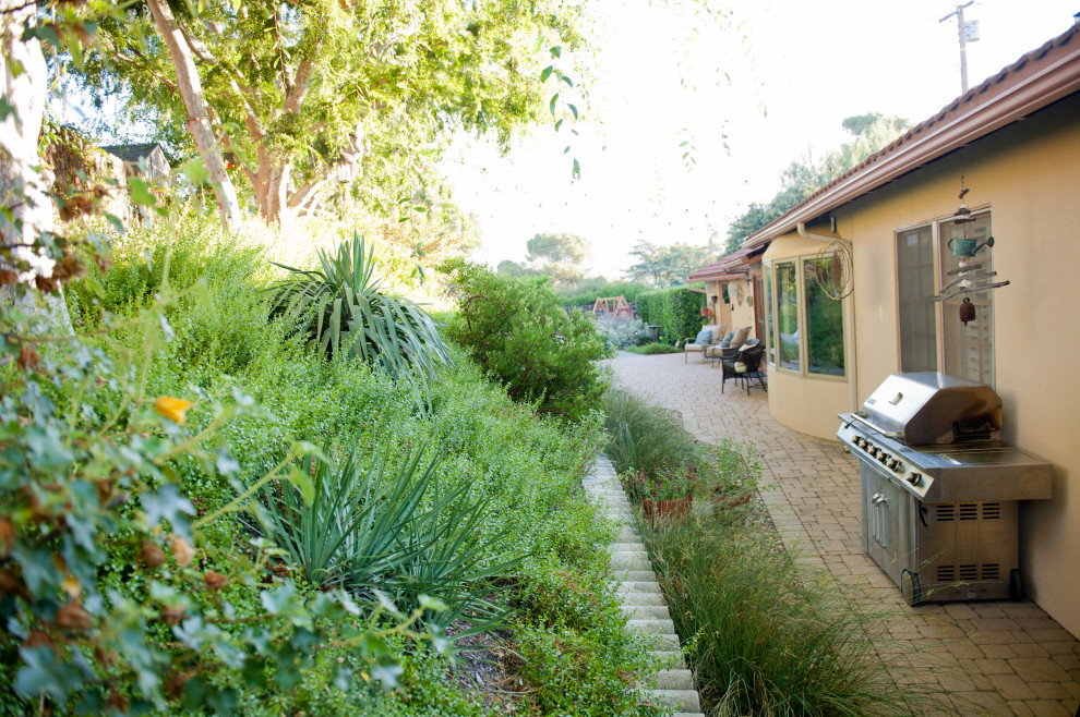 This is an example of an expansive bohemian back xeriscape partial sun garden for spring in Los Angeles with a pathway and brick paving.