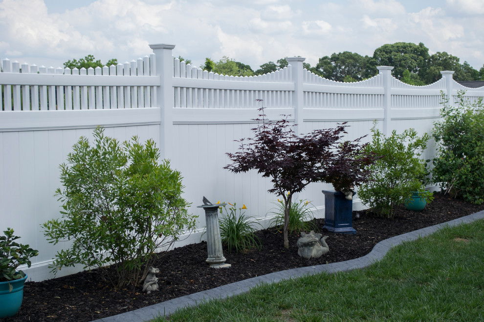 Cette image montre un grand jardin à la française arrière traditionnel au printemps avec une exposition ensoleillée, un paillis et une clôture en vinyle.
