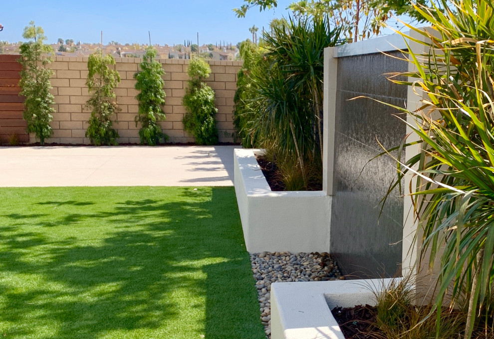 Mittelgroßer Moderner Gartenwasserfall hinter dem Haus mit direkter Sonneneinstrahlung und Betonboden