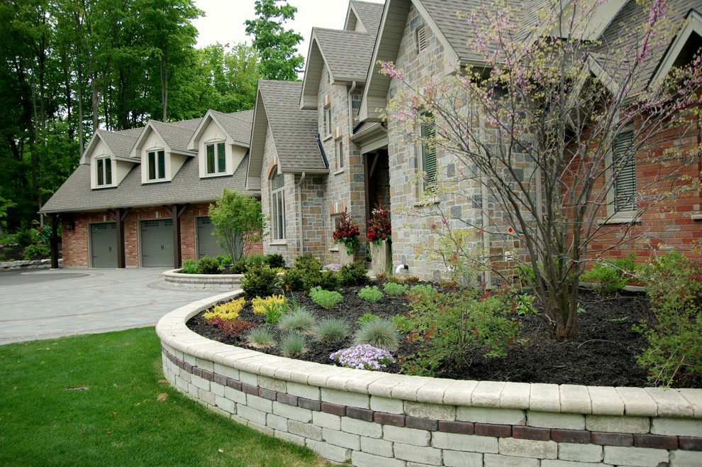 Foto på en stor funkis trädgård framför huset, med marksten i betong och en stödmur