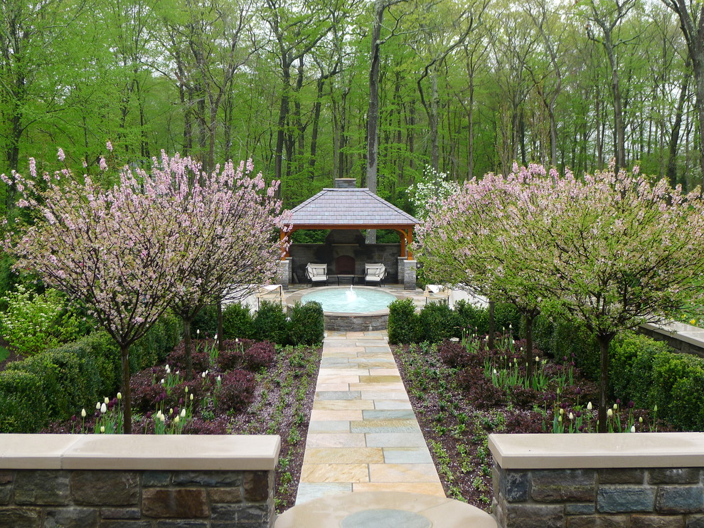 Exempel på en mycket stor klassisk trädgård i skuggan längs med huset på sommaren, med en trädgårdsgång och naturstensplattor